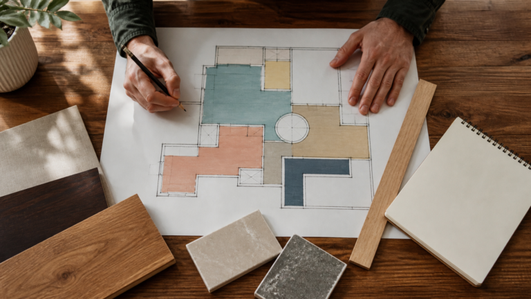 A person marking coloured sections on an irregular floor plan beside material samples